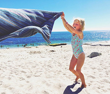Young girl in swimming costume shaking a towl on the beach